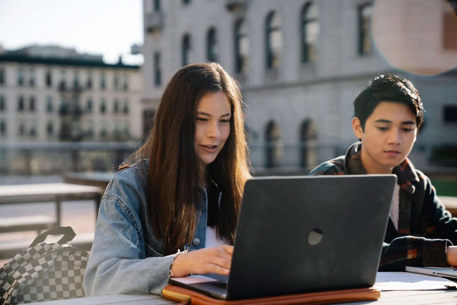 Hai bạn trẻ ngồi cạnh nhau cùng xem bài trên laptop